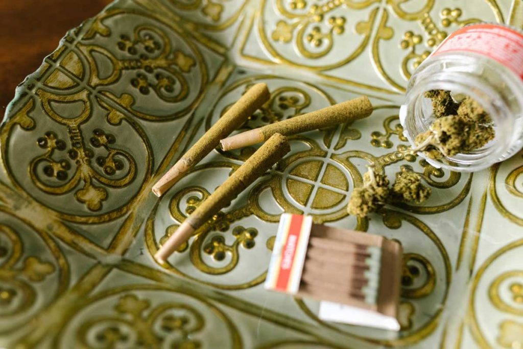 Rolled blunts laying on gilded background with matchbook and jar of weed.
